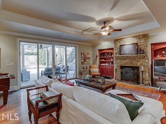 Cozy living room featuring a white sectional sofa, wooden armchair, stone fireplace with a TV, and large glass doors leading to an outdoor space, emphasizing a warm and inviting atmosphere.