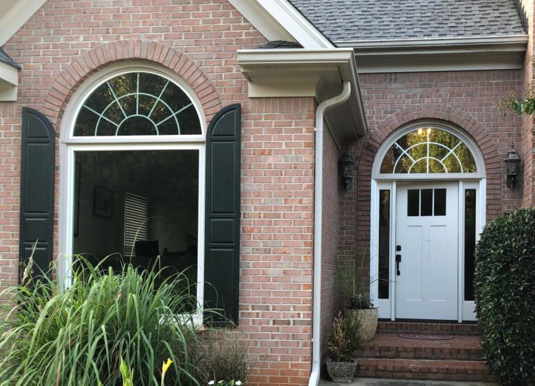 Vinyl single-hung window with half-round top, black shutters, and brick exterior, showcasing energy-efficient design and custom options from Windowcrafters.