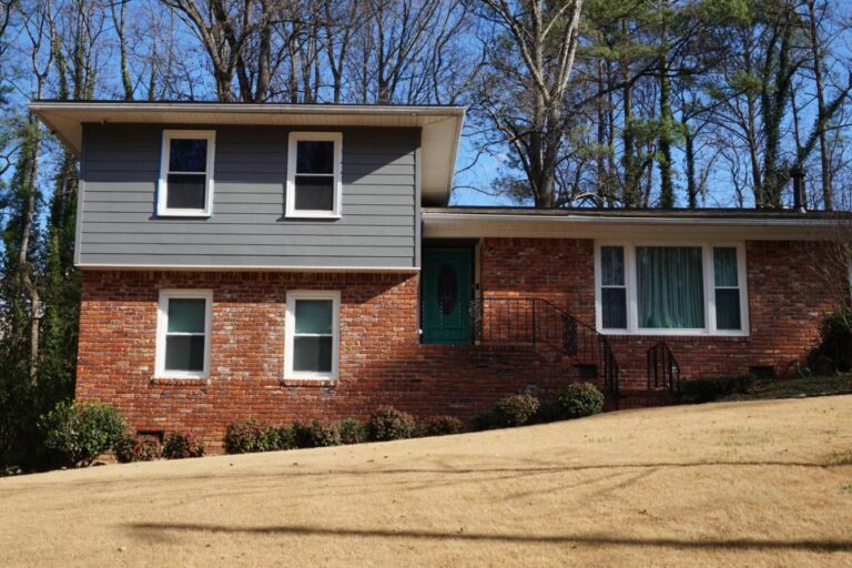 Residential home featuring double-hung vinyl windows, brick facade, and green front door, set in a landscaped yard.