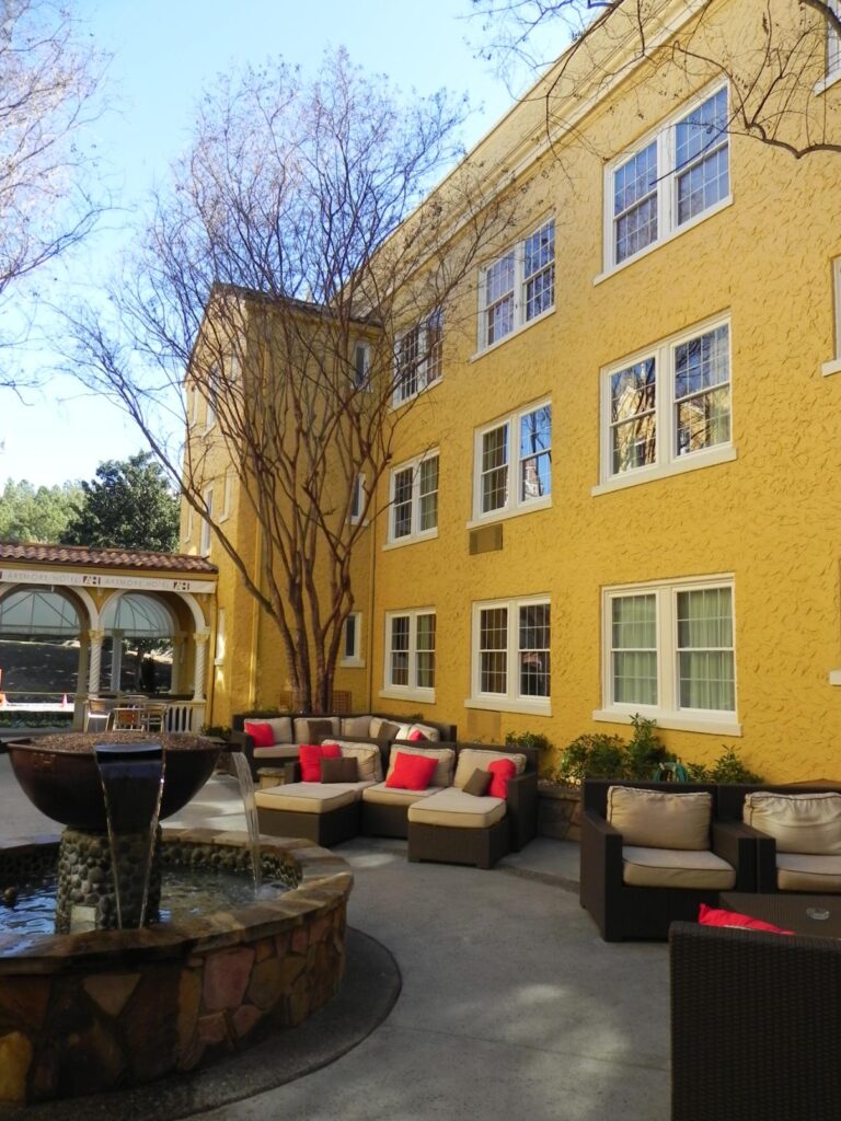 Exterior view of a yellow building featuring double-hung vinyl windows, surrounded by a landscaped area with a water fountain and outdoor seating, emphasizing comfort and aesthetic appeal.