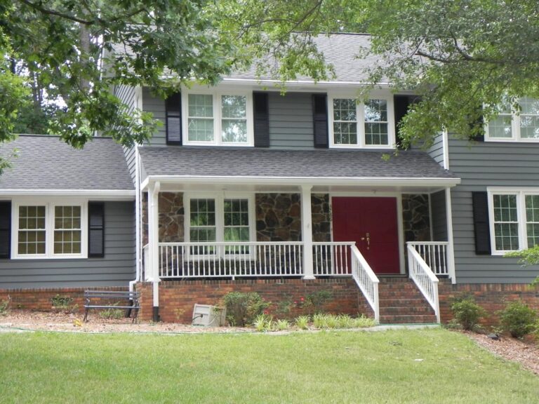 Exterior view of a two-story home featuring 700 Series double-hung vinyl windows, a red front door, and a welcoming porch, surrounded by greenery and landscaping.