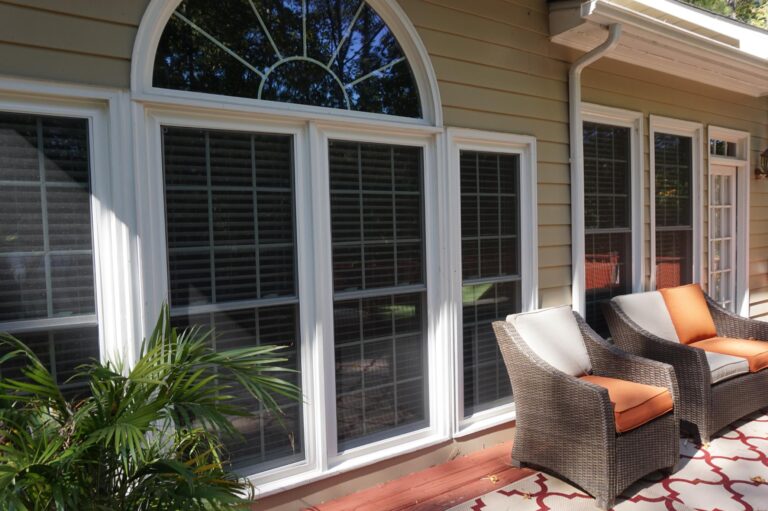 Double-hung vinyl windows with energy-efficient glass in a home setting, featuring white frames and decorative arch above, alongside outdoor seating on a patio.