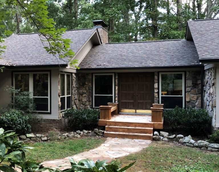 Home exterior featuring double-hung vinyl windows, stone accents, and wooden front steps, surrounded by greenery, showcasing a modern and inviting entrance.