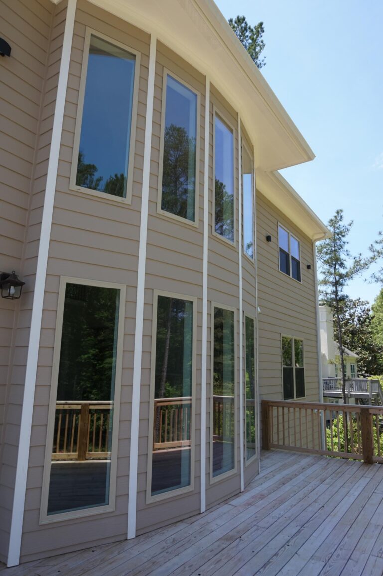 Modern home exterior featuring multiple large vinyl windows, showcasing energy-efficient design and custom-built aesthetics, surrounded by a wooden deck and natural greenery.
