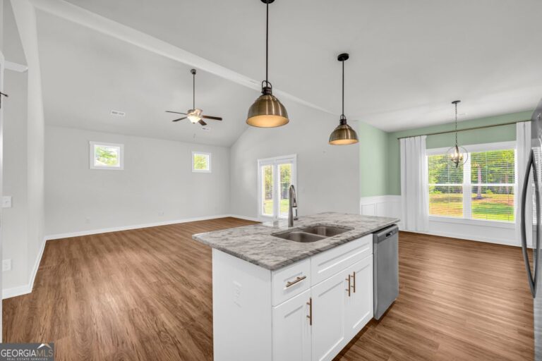 Modern kitchen interior featuring white cabinetry, granite countertops, and stainless steel appliances, with pendant lighting and large windows providing natural light.