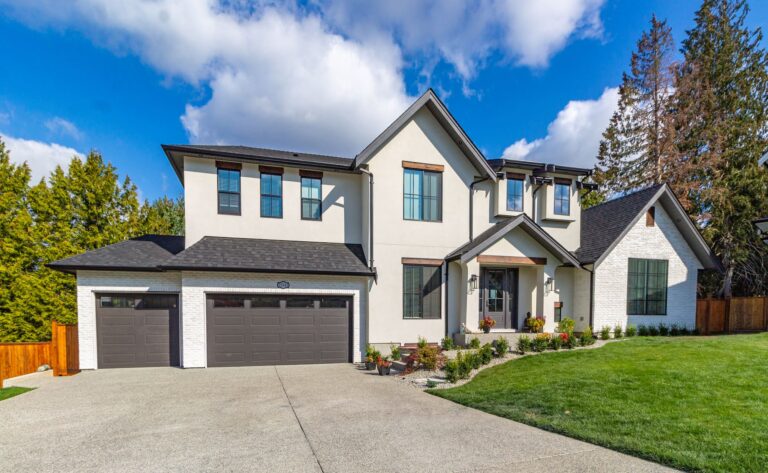 Modern residential home with vinyl windows, two-car garage, landscaped front yard, and blue sky.