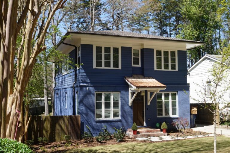 Blue two-story house featuring large vinyl windows, a welcoming front porch with a copper awning, surrounded by a landscaped yard, showcasing quality craftsmanship and energy-efficient design.