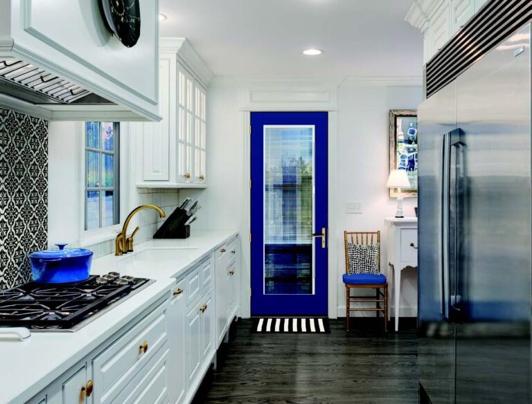 Modern kitchen featuring a blue exterior door with glass panel, white cabinetry, stainless steel appliances, and black and white striped rug, emphasizing custom design and quality craftsmanship.