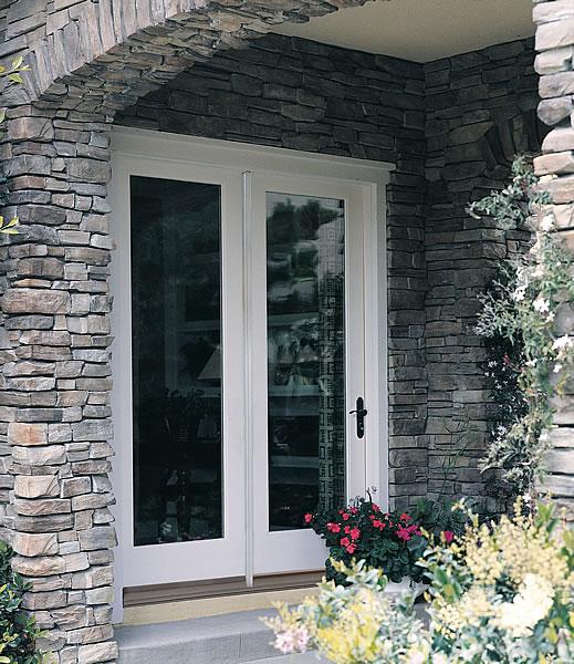 Hinged patio doors framed by stone architecture, surrounded by colorful flowers, showcasing energy-efficient design and aesthetic appeal for exterior home entry.
