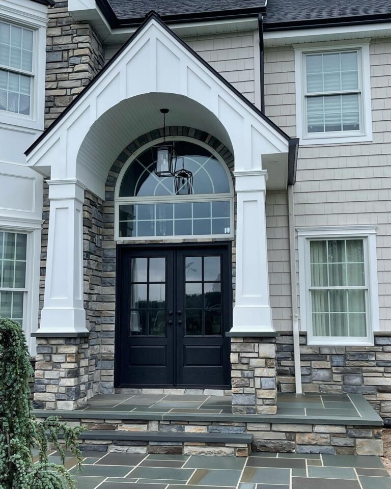 Elegant exterior view of a home featuring a double door entryway with glass panels, stone accents, and a covered porch, showcasing custom exterior doors by Windowcrafters.