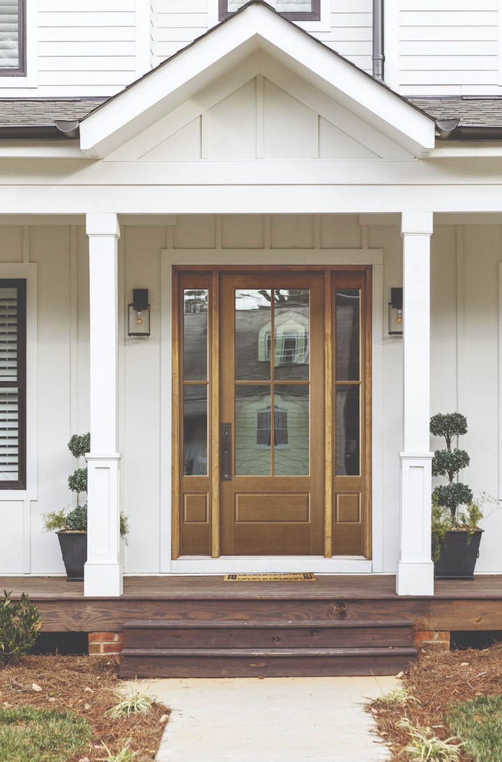 Exterior view of a modern home entrance featuring a double wooden door with glass panels, flanked by decorative plants in pots and a welcoming doormat, emphasizing quality and design in exterior doors.