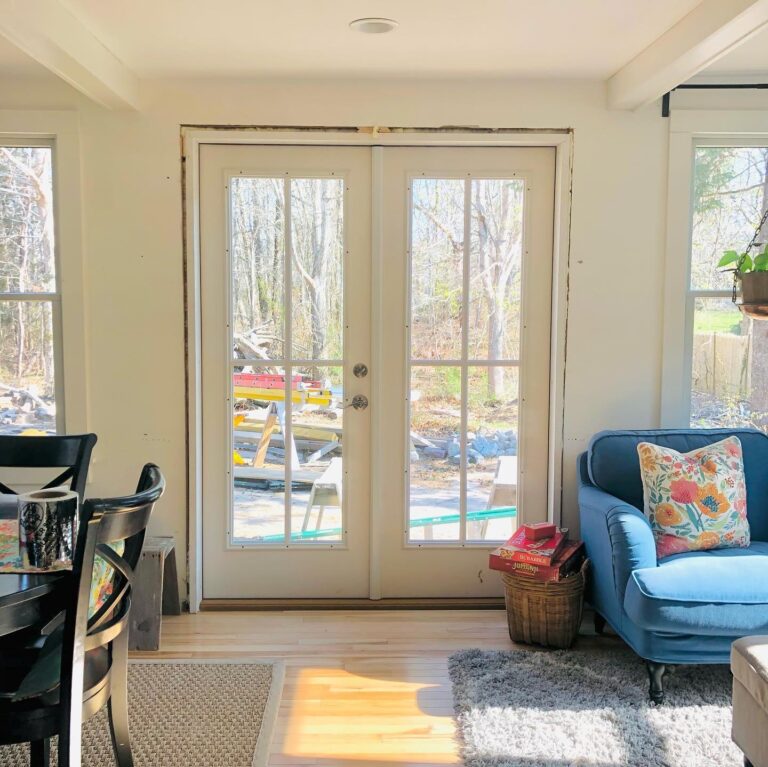 Double French doors leading to an outdoor space, surrounded by natural light, with a cozy blue sofa and dining area visible, emphasizing Windowcrafters' custom door solutions.