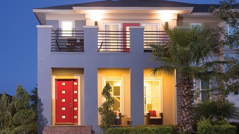 Modern home exterior featuring a vibrant red fiberglass entry door, surrounded by lush greenery and illuminated by warm lighting, showcasing stylish design options available from Windowcrafters.