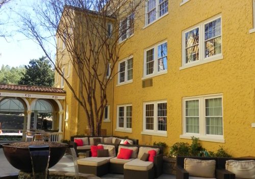 Yellow multi-story building with custom vinyl windows, outdoor seating area featuring cushions, and a landscaped courtyard, showcasing a property ideal for multifamily living and quick window replacements.