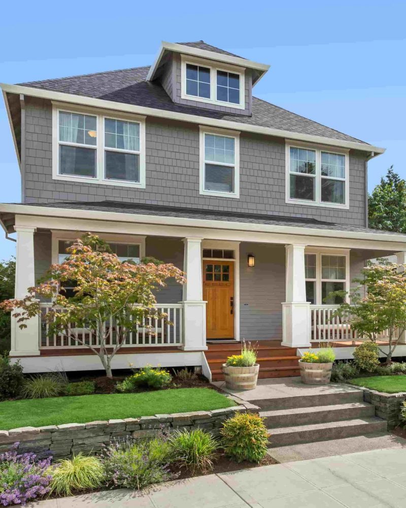 Modern two-story house with vinyl windows, welcoming front porch, landscaped garden, and stone retaining wall, showcasing quality craftsmanship relevant to contractor projects.