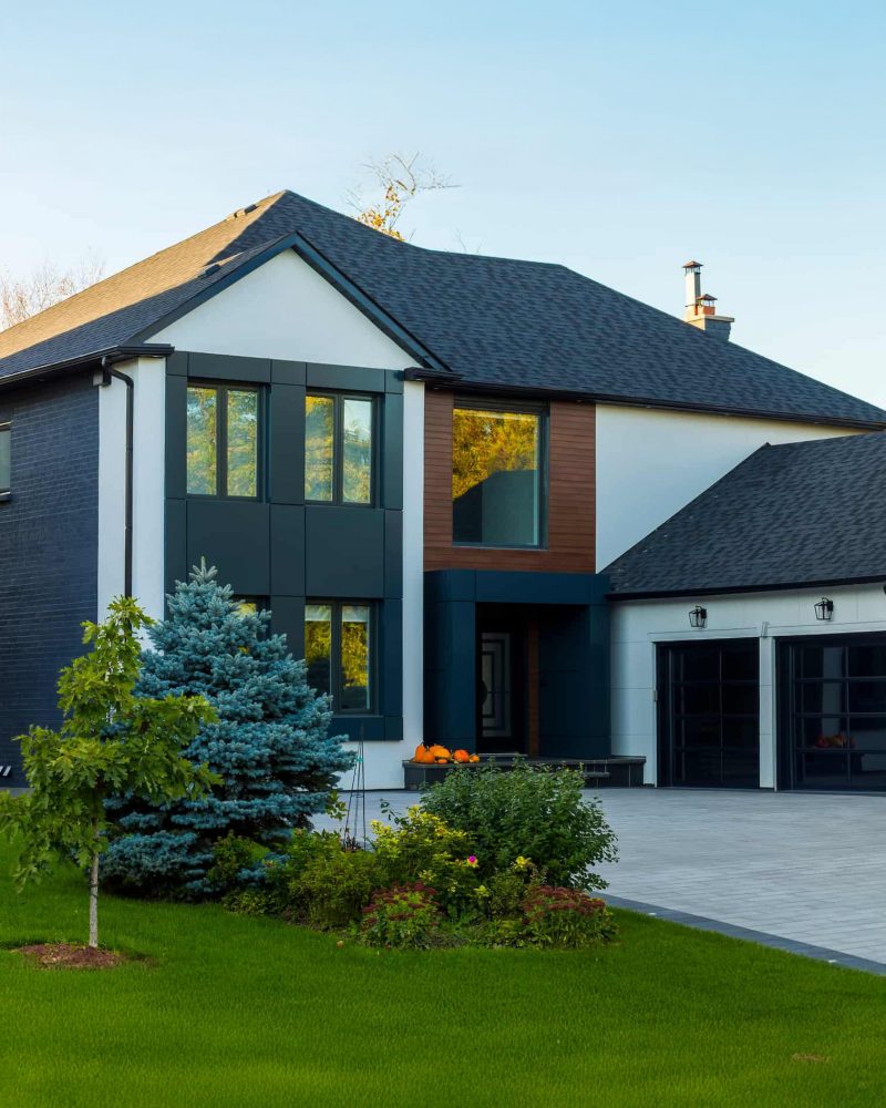 Modern home exterior featuring large vinyl windows, landscaped yard with trees and flowers, and a driveway, emphasizing quality craftsmanship for contractors.