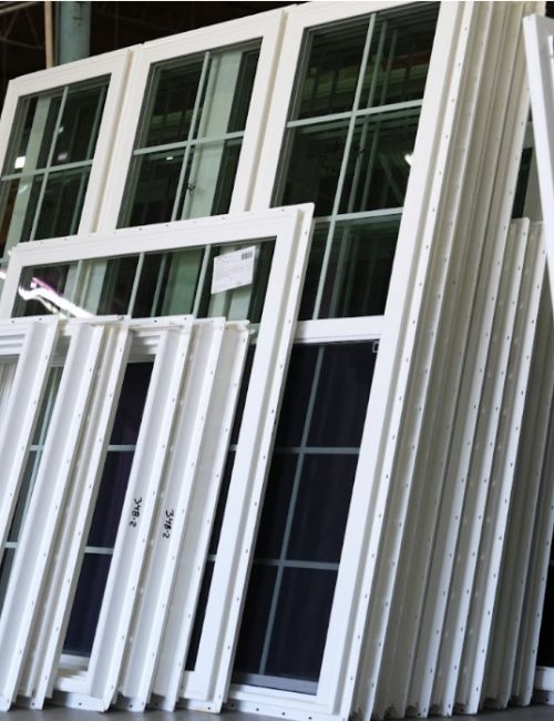 Stack of factory-direct, white vinyl windows with energy-efficient glass, showcasing various sizes and styles for new construction by Window Crafters.