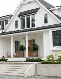 Modern farmhouse exterior featuring large windows, wooden front door, and landscaped entryway with potted plants and seating, showcasing a welcoming design ideal for new construction vinyl window options.