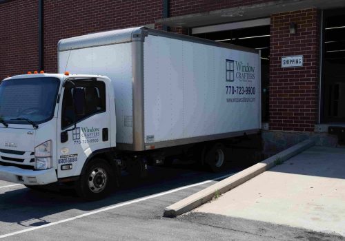 Windowcrafters delivery truck parked at shipping dock, featuring company logo and contact number, emphasizing local manufacturing and reliable service for contractors.