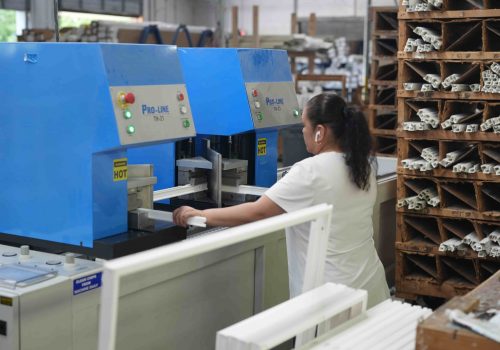 Woman operating machinery in a vinyl window manufacturing facility, showcasing local production for custom and stock window sizes.