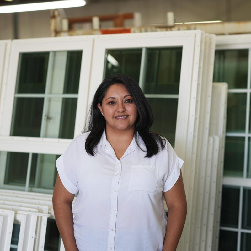 Woman smiling in front of factory-produced vinyl windows, representing Windowcrafters' dedicated team and quality service in Georgia.