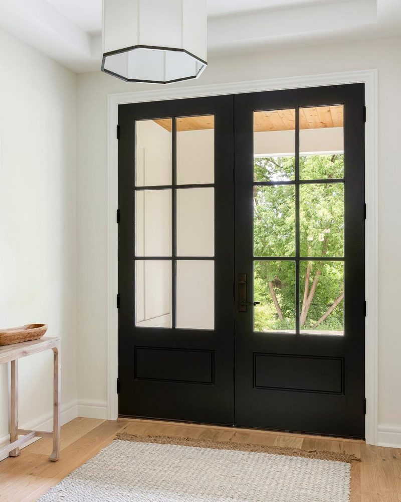 Black fiberglass entry door with glass panels, showcasing energy-efficient design and modern style, set in a bright entryway with natural light and a view of greenery.